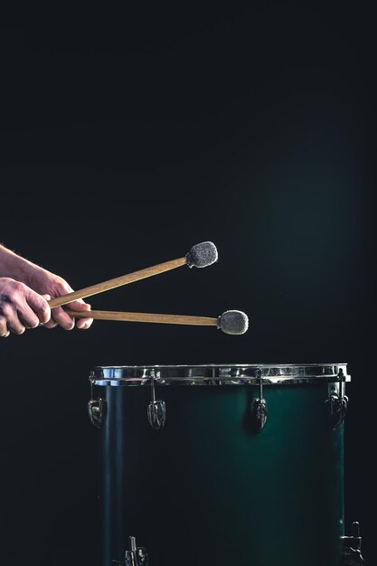 Foto um homem toca um instrumento musical de percussão com paus em um fundo escuro