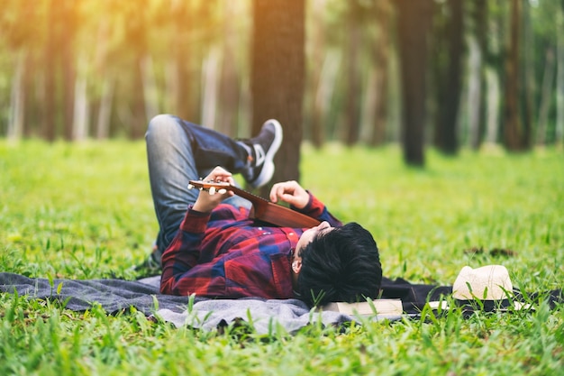 Um homem tocando ukulele deitado em um jardim verde