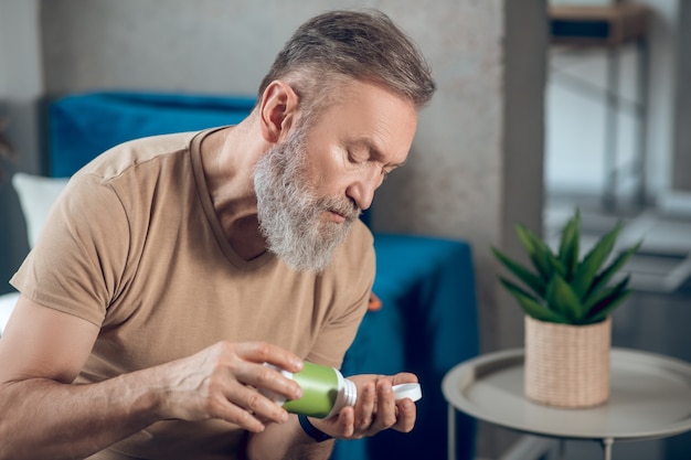 Um homem tomando um comprimido de um frasco verde