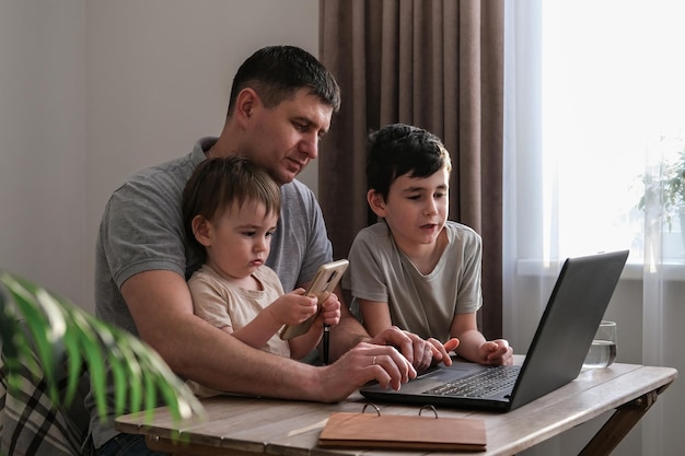 Um homem trabalha em casa com um laptop e cuida das criançasEscritório em casa e paternidade ao mesmo tempo