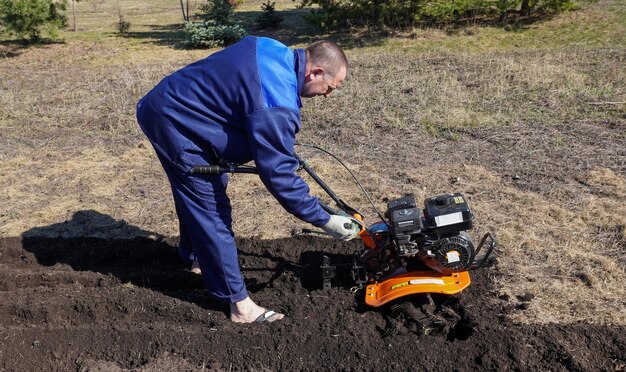 Um homem trabalha numa horta no início da primavera, cava o chão, trabalha como cultivador.