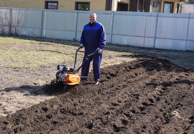 Um homem trabalha numa horta no início da primavera, cava o chão, trabalha como cultivador.