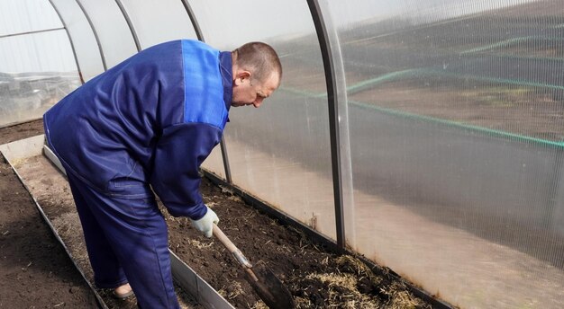 Um homem trabalha numa horta no início da primavera, escava o chão, trabalha numa estufa.