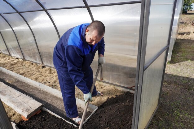 Foto um homem trabalha numa horta no início da primavera, escava o chão, trabalha numa estufa.