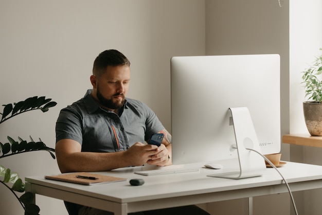 Foto um homem trabalha remotamente em um computador desktop. um cara com barba está navegando nas redes sociais durante uma reportagem de um colega em uma videoconferência em casa. um professor está se preparando para uma palestra online.