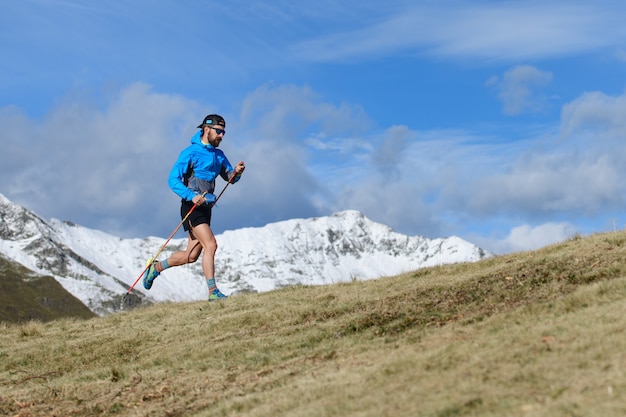 Um homem treina para uma trilha ultra-corrida em um prado montanhoso no outono com a primeira neve nas montanhas