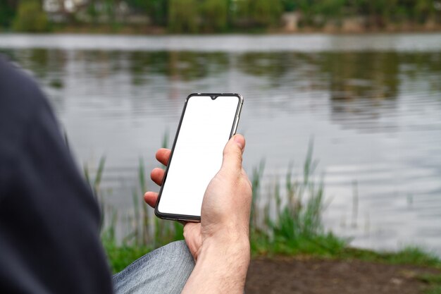 Um homem usa seu smartphone na margem de um lago