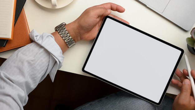 Um homem usa uma caneta stylus para desenhar na tela de um tablet. Maquete de tela em branco do tablet touchpad. vista do topo