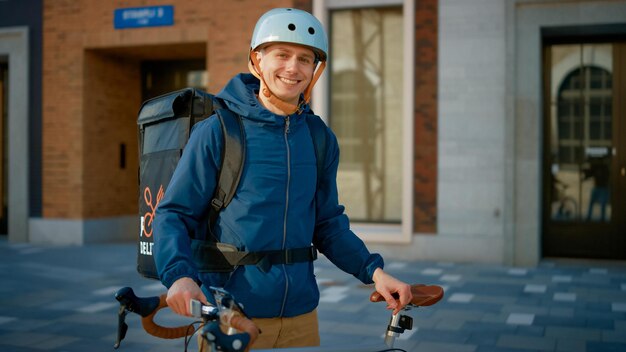 Um homem usando um capacete de entregador de pizza fica ao lado de uma bicicleta com uma placa que diz entrega de pizza.