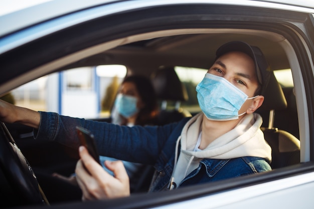 Um homem usando uma máscara médica segura um celular na mão enquanto dirige um carro