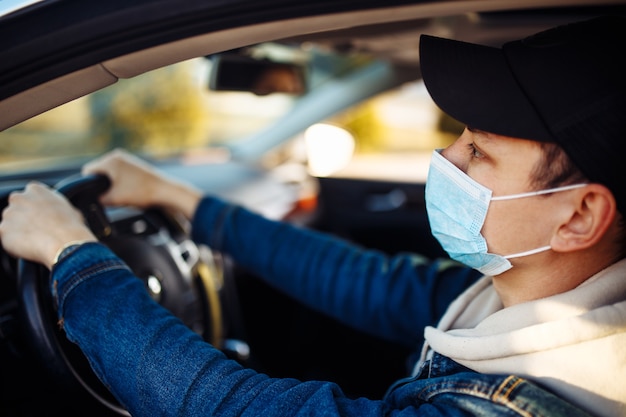 Um homem usando uma máscara médica segura um celular na mão enquanto dirige um carro