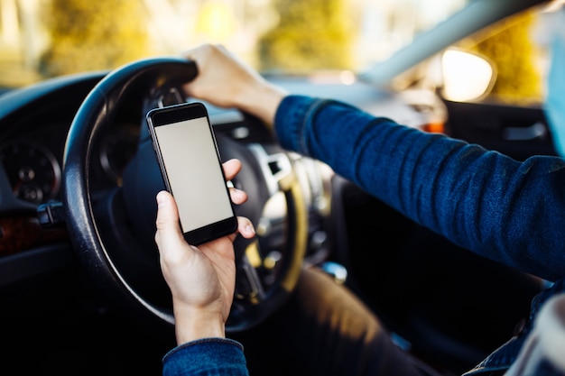 Um homem usando uma máscara médica segura um celular na mão enquanto dirige um carro