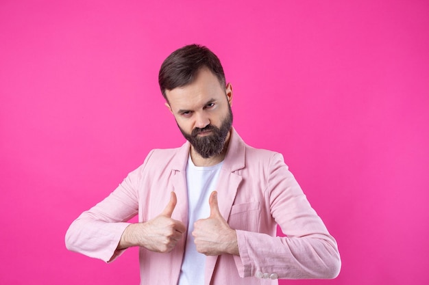 Um homem vestido com uma jaqueta rosa com barba mostra um polegar para cima