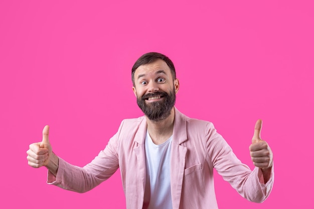 Um homem vestido com uma jaqueta rosa com barba mostra um polegar para cima