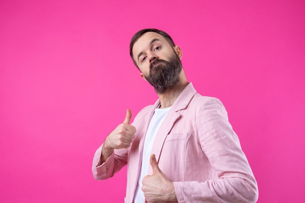 Um homem vestido com uma jaqueta rosa com barba mostra um polegar para cima