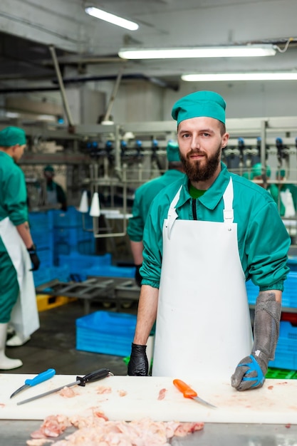 Um homem vestindo um avental branco está em uma fábrica com uma máquina azul ao fundo.