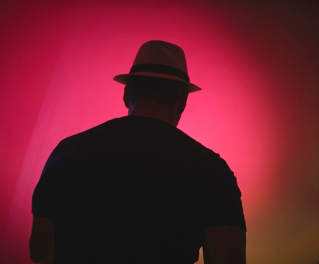 Um homem vestindo um chapéu e uma camisa preta está de pé na frente de um fundo rosa