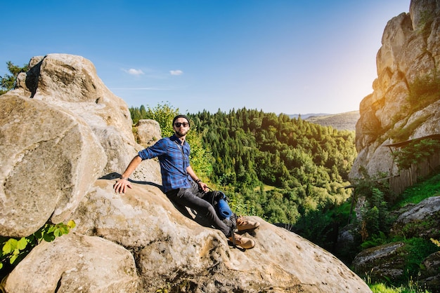 Um homem viajante com mochila e óculos de sol sentado nas rochas nas montanhas