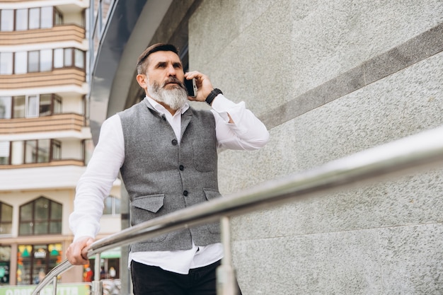 Um idoso barbudo e de cabelos grisalhos usa e fala em um smartphone