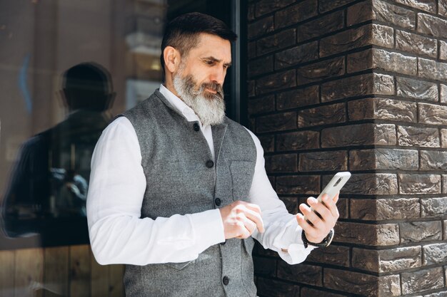 Um idoso barbudo e de cabelos grisalhos usa e fala em um smartphone