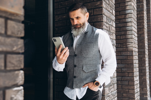 Um idoso barbudo e de cabelos grisalhos usa e fala em um smartphone