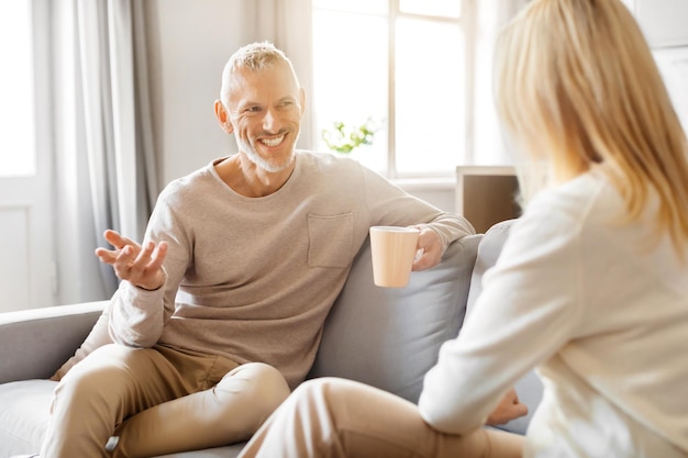 Foto um idoso e uma idosa felizes a beber café e a conversar em casa.