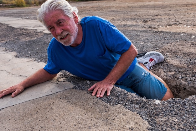Um idoso ou aposentado caiu no chão porque enfiou o pé num buraco na rua - homem maduro precisando de ajuda na estrada - problema para um aposentado
