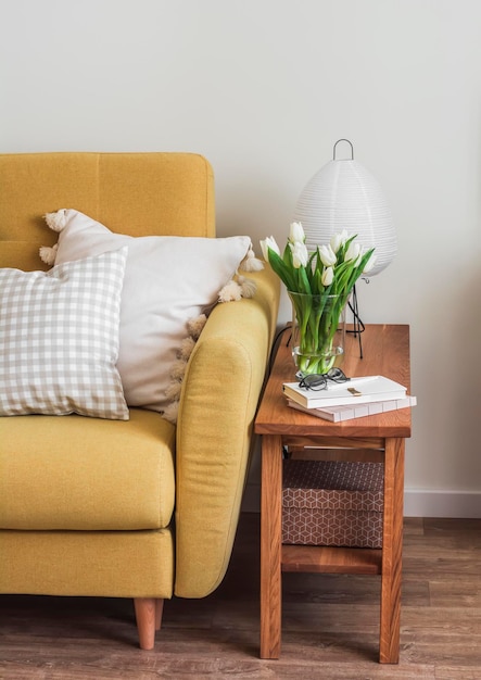 Foto um interior aconchegante um sofá amarelo um banco de madeira com uma lâmpada de papel um buquê de tulipas em um vaso uma revista no interior da sala de estar