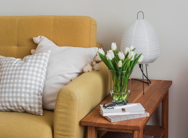 Foto um interior aconchegante um sofá amarelo um banco de madeira com uma lâmpada de papel um buquê de tulipas em um vaso uma revista no interior da sala de estar