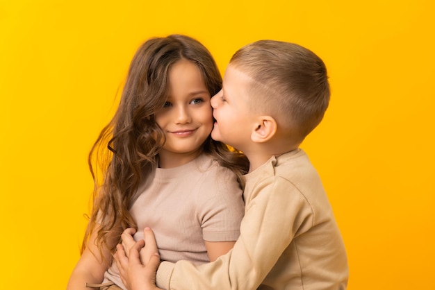 Um irmão mais novo está abraçando e beijando sua irmã mais velha em um fundo amarelo no estúdio