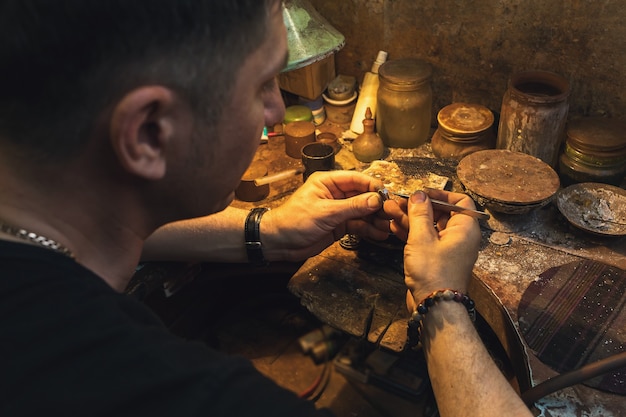 Um joalheiro conserta um anel de ouro com uma pedra em sua oficina