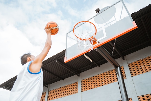 Um jogador de basquete segurando uma bola dá uma tacada no aro