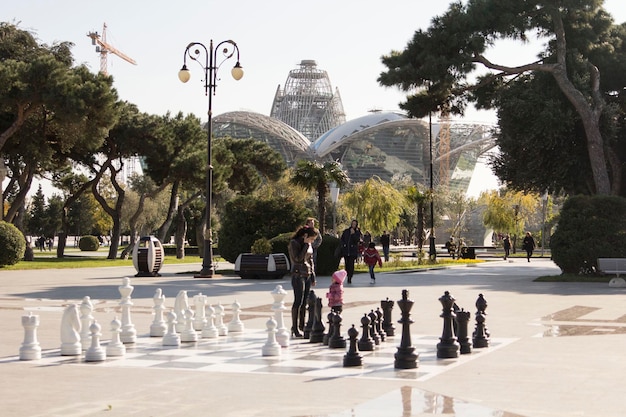 Um jogo de xadrez gigante está montado em uma praça em frente a um grande prédio.