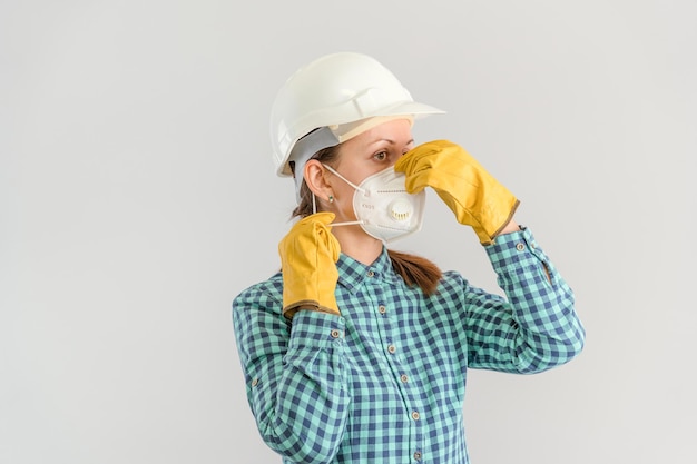 Um jovem adulto trabalhador da construção civil coloca uma máscara médica protetora. Uma engenheira com um capacete de segurança usando um respirador N95 e luvas amarelas. Foto horizontal