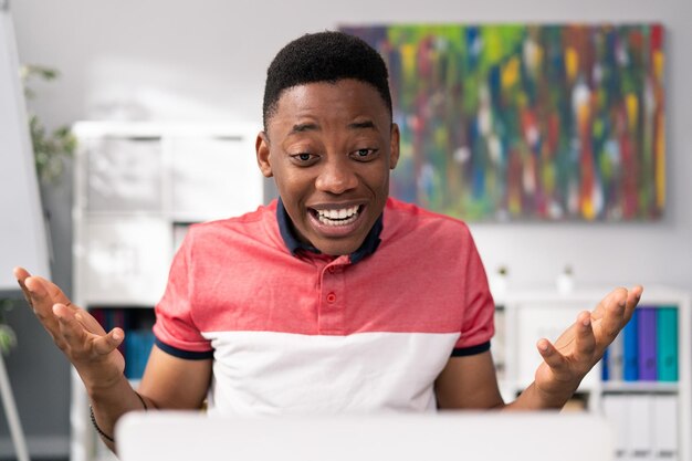 Um jovem africano americano bonito está sentado em uma mesa em uma sala em frente a um laptop