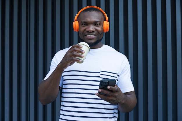 Um jovem afro-americano elegante escuta música em fones de ouvido com um café na mão