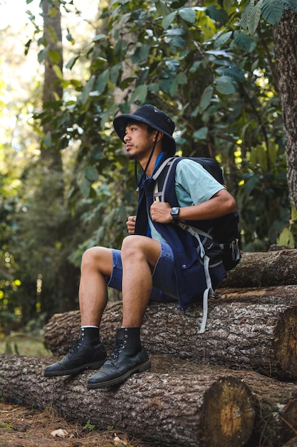 Um jovem alpinista com mochila olhando para longe e sentado em uma pilha de madeira descansando antes