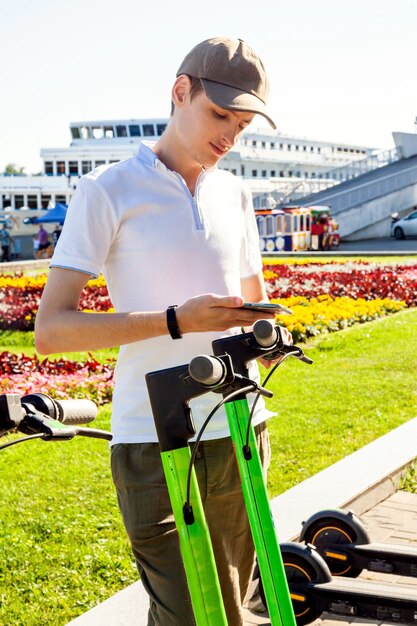 Um jovem aluga uma scooter elétrica digitalizando o código QR com um smartphone. Chute scooters no estacionamento compartilhado.