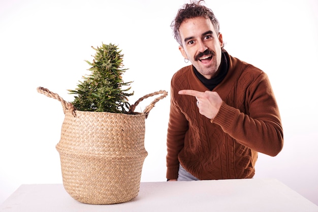 Um jovem apontando o dedo para uma planta de cannabis com fundo branco