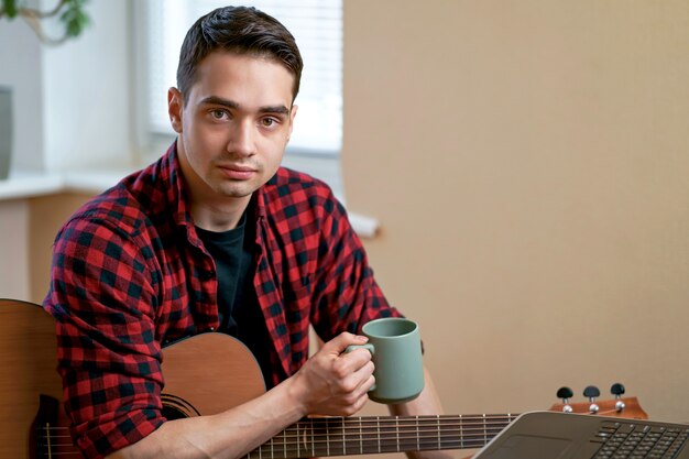 Um jovem aprende a tocar violão usando a Internet, um laptop, uma aula online