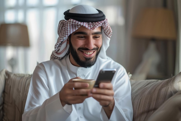 Um jovem árabe bonito e sorridente segura um smartphone enquanto desfruta de uma chávena de chá ou café no