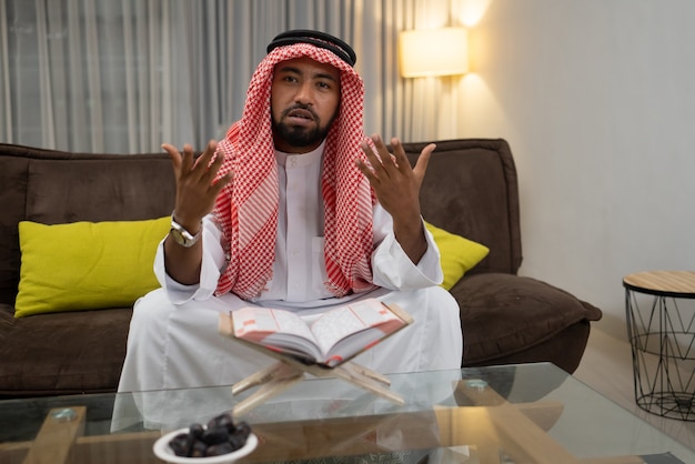 Um jovem árabe lendo o Alcorão com a expressão de suas mãos olhando para cima