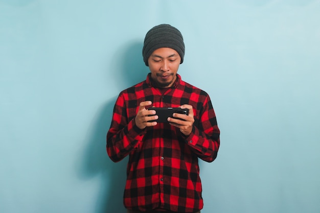Um jovem asiático animado está jogando um jogo online em seu smartphone isolado em um fundo azul