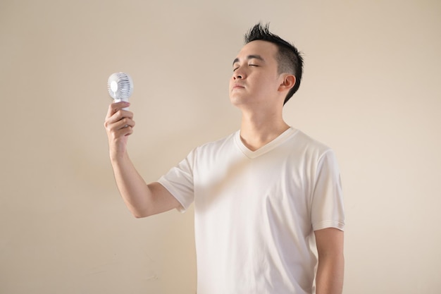 Foto um jovem asiático está usando um ventilador portátil por causa do calor