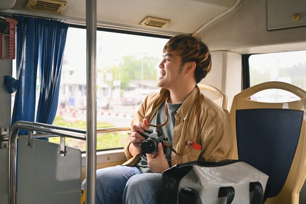 Um jovem asiático sorridente a viajar de transporte público e a olhar pela janela.