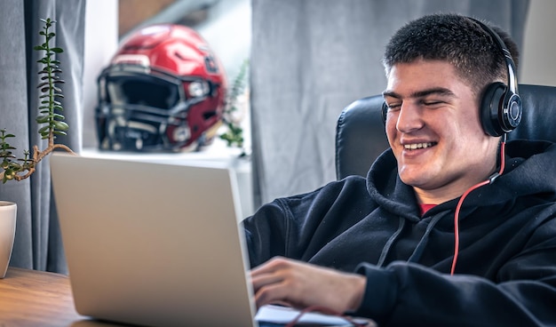 Um jovem atleta do sexo masculino se senta na frente de um laptop em seu quarto