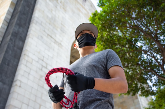 Um jovem atleta usando uma máscara e segurando uma corda de pular na rua