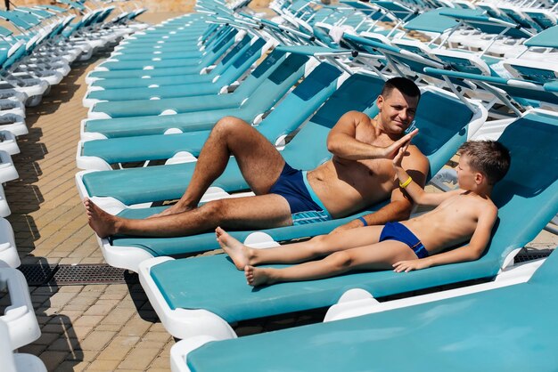 Um jovem atlético e seu filho estão sorrindo alegremente e tomando sol em uma espreguiçadeira em um dia ensolarado no hotel Boas férias em família em um hotel no resort Férias de verão e turismo