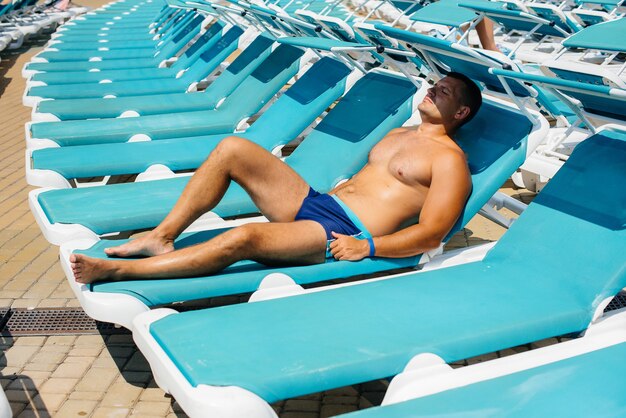 Um jovem atlético está sorrindo alegremente e tomando banho de sol em uma espreguiçadeira em um dia ensolarado. Boas férias de férias. Férias de verão e turismo.