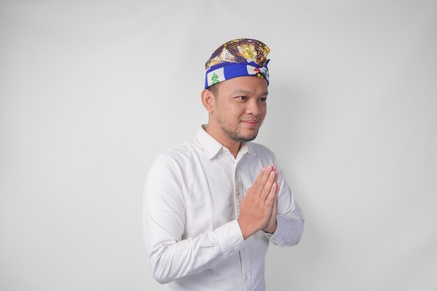 Foto um jovem balinês sorridente vestindo um chapéu tradicional chamado udeng fazendo um gesto de saudação ou bem-vindo isolado sobre um fundo branco